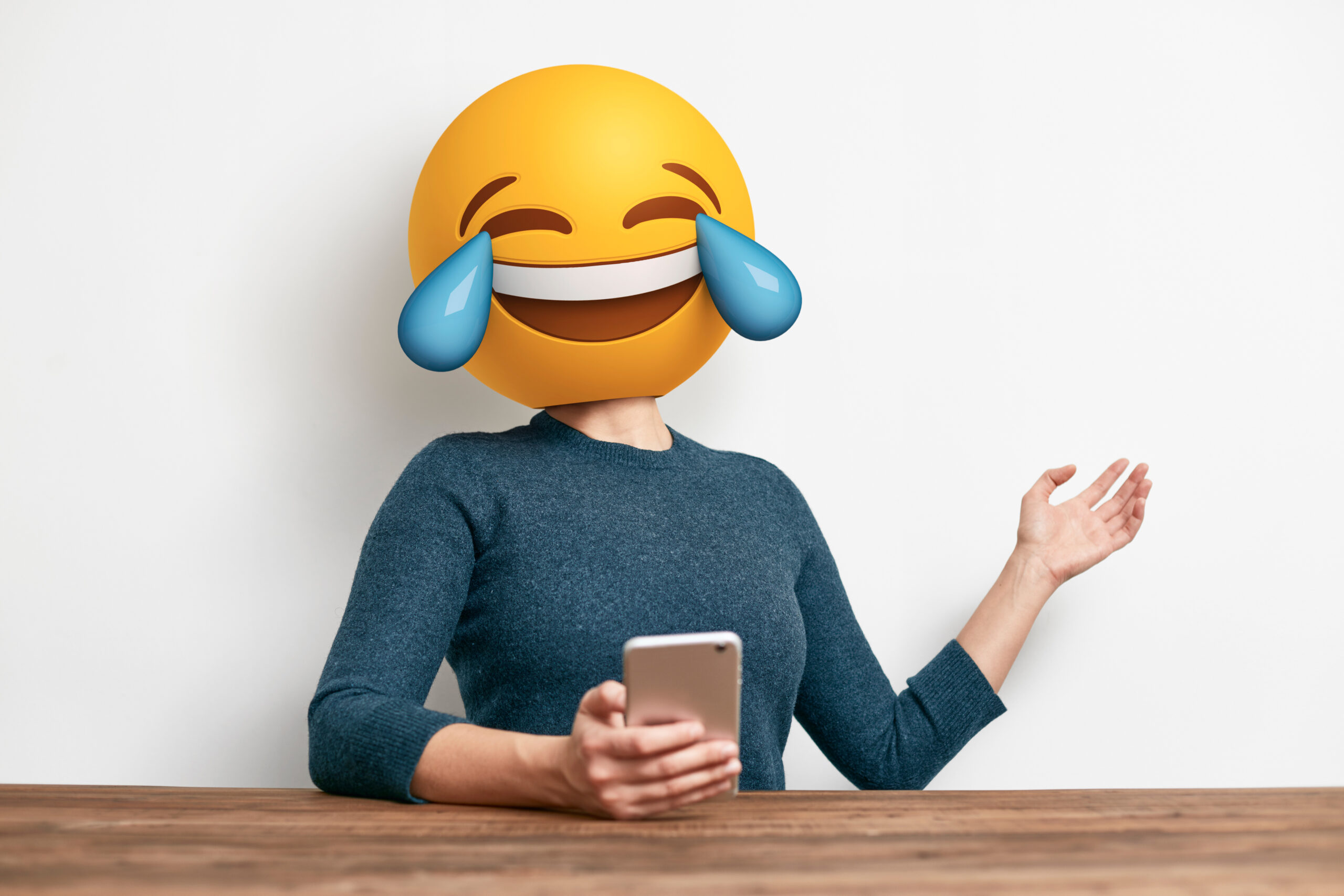 Frau mit Handy in der Hand und Lach-Emoji als Kopf